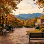 Sunlight filters through autumn trees onto a historic brick town square with inviting benches, framed by rolling blue mountains in the distance